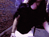 a woman in a black shirt is standing in front of a brick wall with graffiti on it .