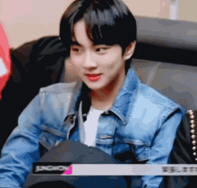 a young man wearing a blue denim jacket is sitting in a chair
