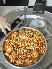 a bowl of noodles sits on a silver tray next to a phone