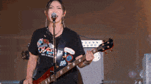 a woman is singing into a microphone while playing a guitar and wearing a shirt that says over
