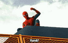 a man in a spiderman costume is sitting on top of a fence with the word yoink on it .