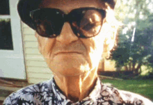 an elderly man wearing sunglasses and a hat looks at the camera