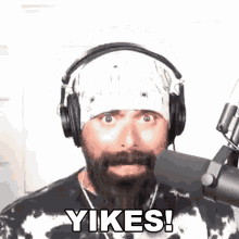 a man with a beard and headphones is standing in front of a microphone and saying yikes .