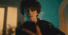 a young man with curly hair is standing in front of a window and making a funny face .
