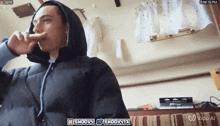 a man wearing a hooded jacket is talking on a cell phone and the time is 2:16