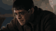 a close up of a man wearing glasses and a brown shirt .