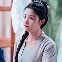 a woman with braided hair and a flower in her hair looks to the side