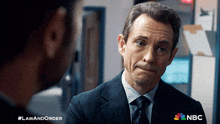 a man in a suit and tie is talking to another man with the nbc logo behind him
