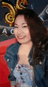 a woman wearing a denim jacket and a blue dress is smiling in front of balloons .