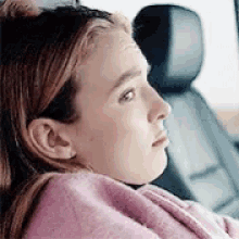 a young girl is sitting in the back seat of a car with a pink blanket on her head .