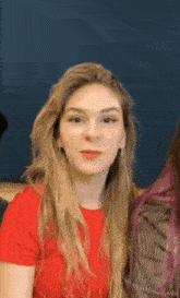a woman with long blonde hair is wearing a red shirt and looking at the camera .