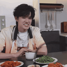 a young man wearing a shirt that says bofe sits at a table eating food