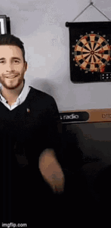 a man is standing in front of a dart board on a wall and smiling .