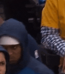 a man wearing a blue hoodie and a hat is sitting in a crowd .
