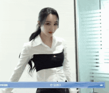 a woman wearing a white shirt and a black top is standing in front of a glass door with a blue box that says yeon