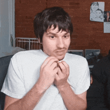 a man in a white shirt is making a face in front of a brick wall