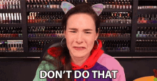 a woman wearing cat ears is sitting in front of a wall of nail polish and says don 't do that .