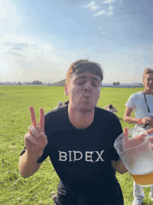 a man wearing a black t-shirt that says bidex blowing a peace sign