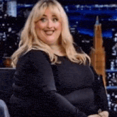 a woman is sitting in a chair and smiling . she is wearing a black shirt .