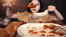 a woman in a plaid shirt is eating food with a spoon