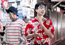 a man wearing a face shield and a hawaiian shirt stands next to another man