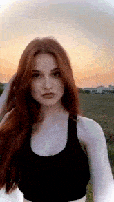 a woman with red hair is wearing a black crop top and standing in a field .