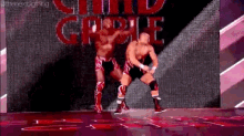 two wrestlers are dancing on a stage in front of a large screen with the word castle on it .