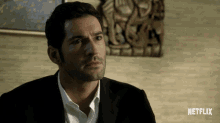 a man in a suit and white shirt is sitting in front of a netflix sign