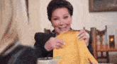a woman is sitting at a table holding a piece of yellow fabric .