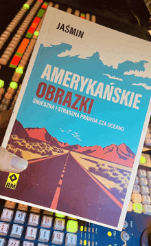 a book titled amerykańskie obrazki is being held in front of a keyboard