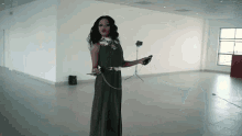 a woman in a long dress is standing in an empty room holding a remote control .