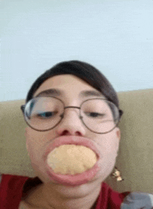 a woman wearing glasses is making a funny face while holding a piece of food in her mouth .