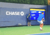 a man stands on a tennis court in front of a chase wall