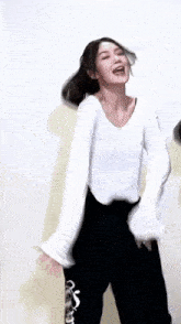 a woman in a white shirt and black pants is dancing and making a funny face .