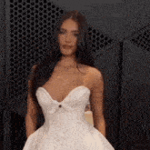 a woman in a white wedding dress is standing in front of a black wall .