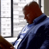 a man in a blue suit is reading a book while sitting in front of a window .