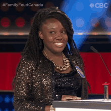 a woman in a sequined jacket stands in front of a podium with a cbs logo on the bottom