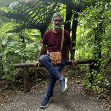 a man sits on a wooden railing in the woods with his legs crossed