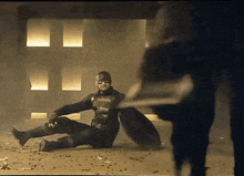 a man in a superhero costume is sitting on the ground holding a shield .