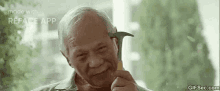 an elderly man is holding a hammer to his ear and smiling .