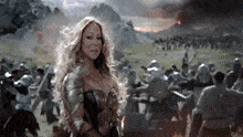 a woman in armor stands in front of a crowd of soldiers .