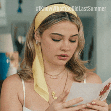 a woman wearing a yellow headband and a necklace looks at a piece of paper