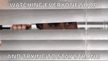 a man is peeking through the blinds of a window and trying to stay strong .
