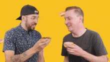 two men eating donuts on a yellow background with donuts falling around them
