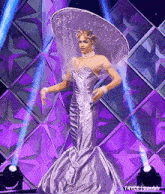 a woman in a purple dress and a white hat is standing on a stage .