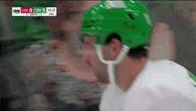 a hockey player wearing a green helmet is looking at the scoreboard