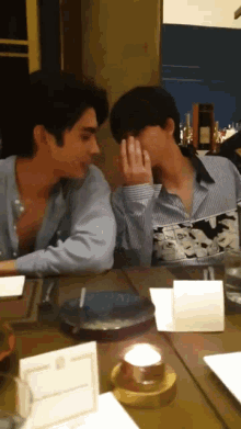 two men are sitting at a table with a candle in the middle of the table