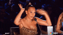 a woman in a leopard print dress is sitting in front of a microphone with the nbc logo in the background