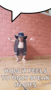 a little boy wearing a cowboy hat and glasses is dancing in front of a pink brick wall .