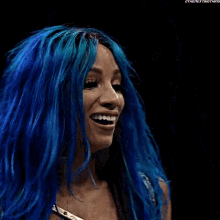 a woman with blue hair is smiling and wearing a black and gold top .